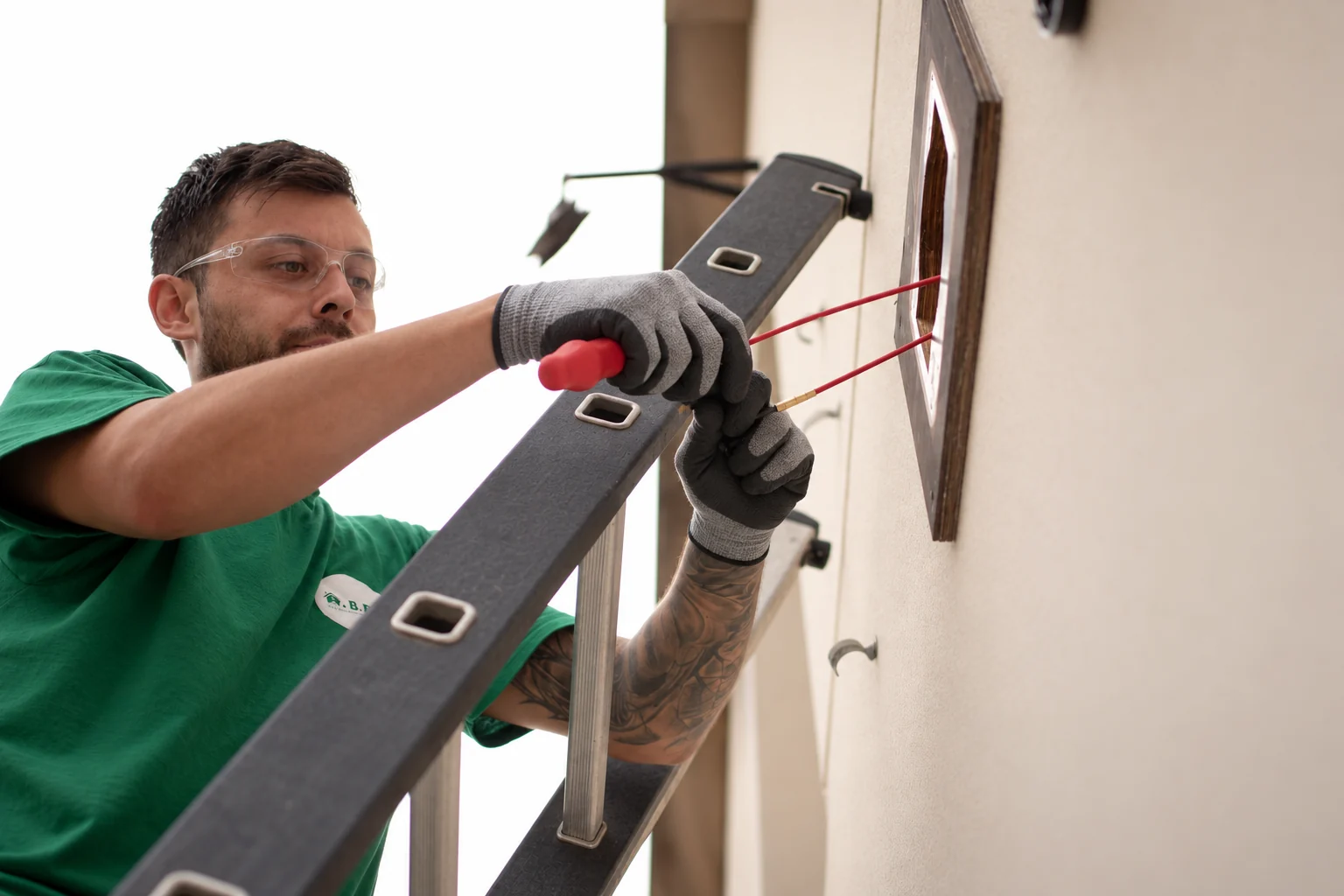 Close-up of a member of the A.BEC team working with tools and wires beside a ladder.